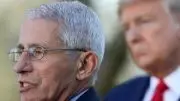 fauci in a suit and light blue shirt speaking outside with trump listening in the background