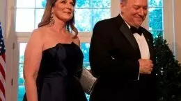susan and mike pompeo, dressed in black tie, walk past a flag