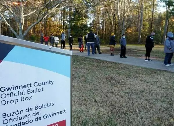 an absentee ballot drop box is in the foreground in georgia, while voters stand in line in the background.